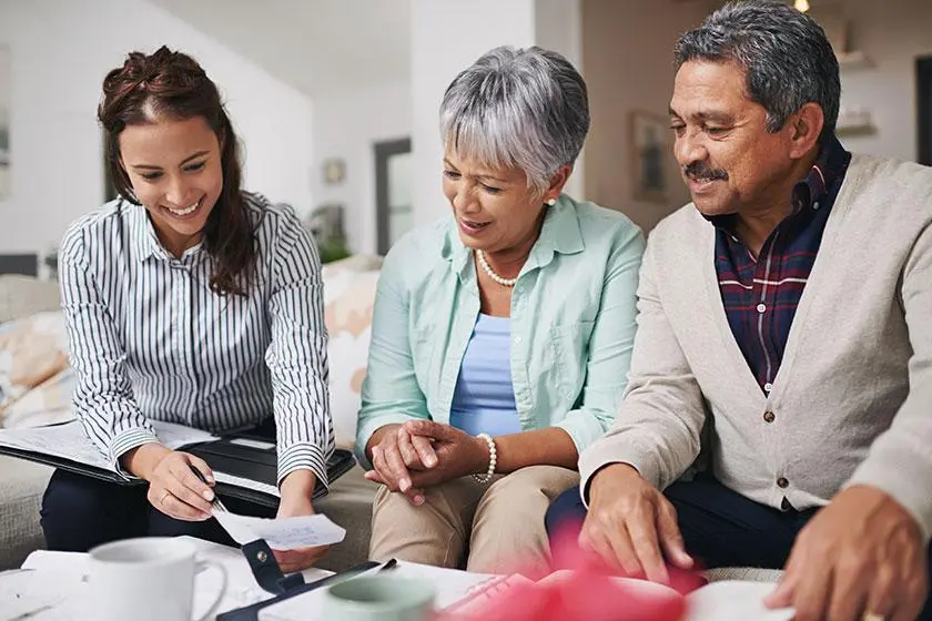 An adult daughter reviews care paperwork with her parents around the kitchen table.